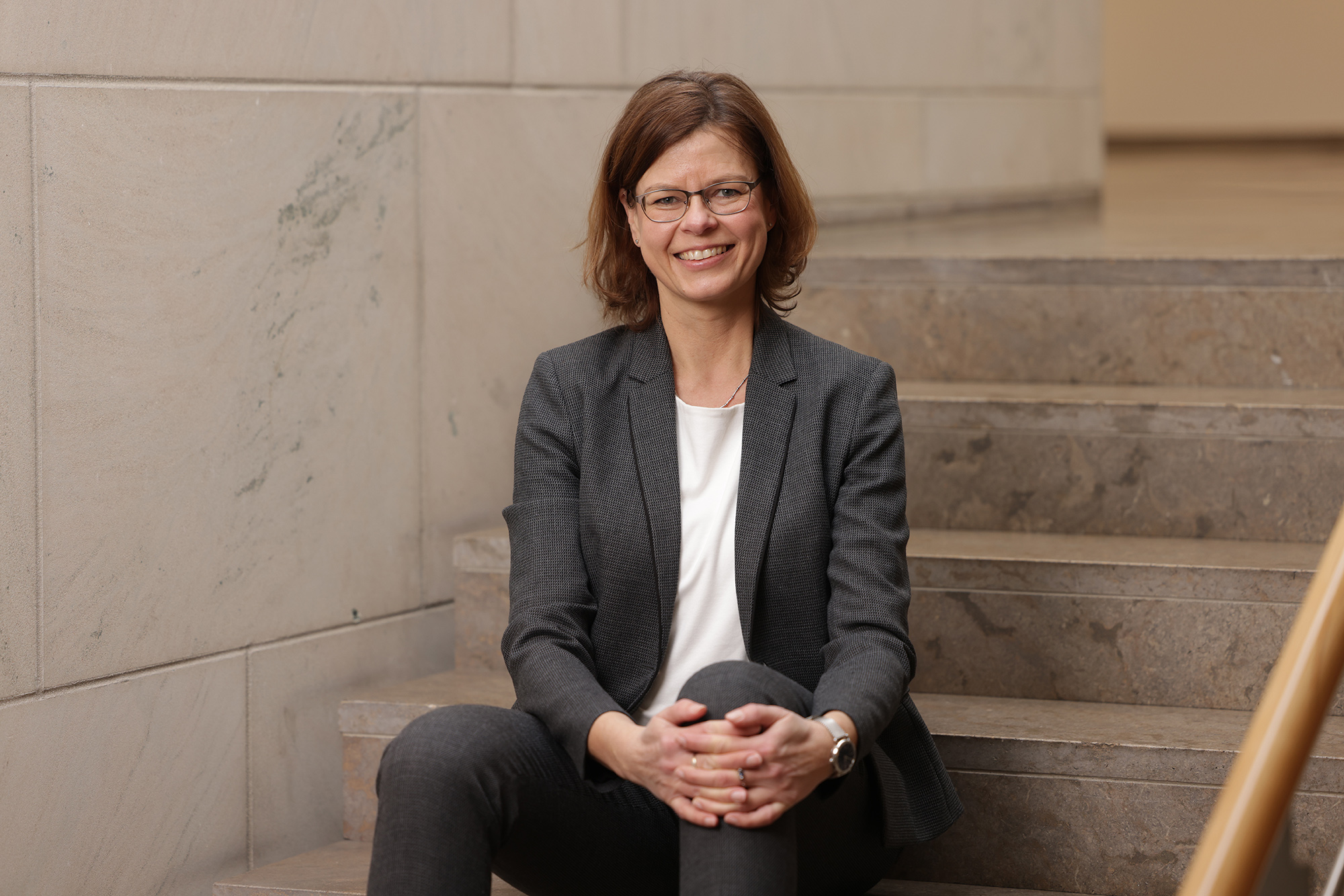 Prof. Anja Schulz sitzt auf einer Treppe un dlächelt in die Kamera