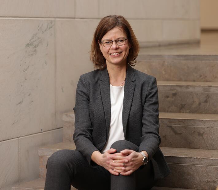 Prof. Anja Schulz sitzt auf einer Treppe un dlächelt in die Kamera