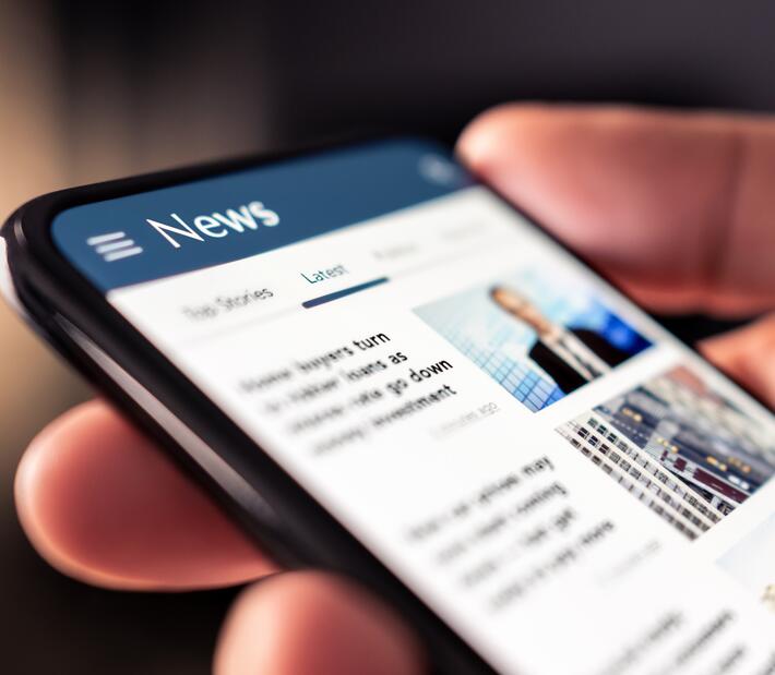 Smartphone liegt in einer Hand und zeigt Newsartikel an
