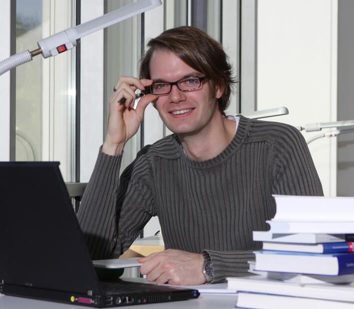 Ein Mann sitzt mit Laptop und Büchern am Schreibtisch
