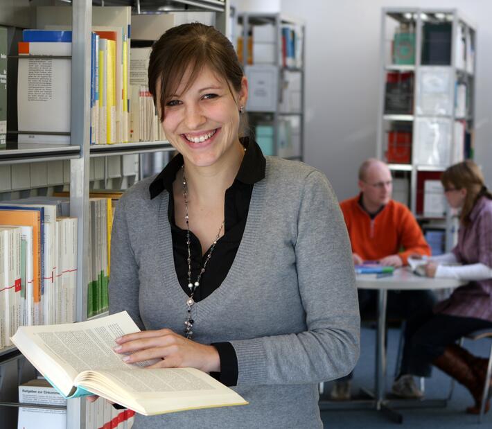 Eine Frau hält ein Buch in den Händen und lächelt in die Kamera