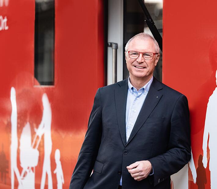 Ein Mann im Anzug steht vor einem roten Hintergrund