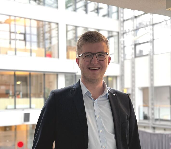 Ein junger Mann im Anzug lächelt in die Kamera