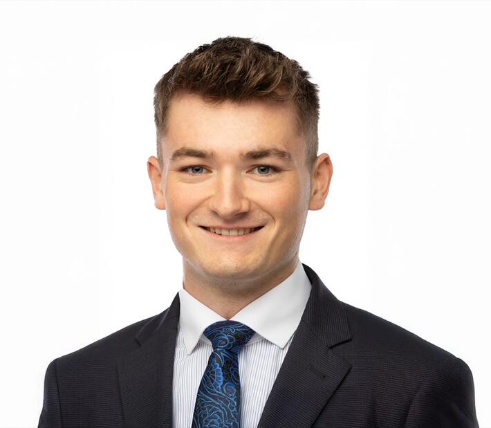 Student im Business Management im Anzug mit Krawatte lächelnd vor weißem Hintergrund.