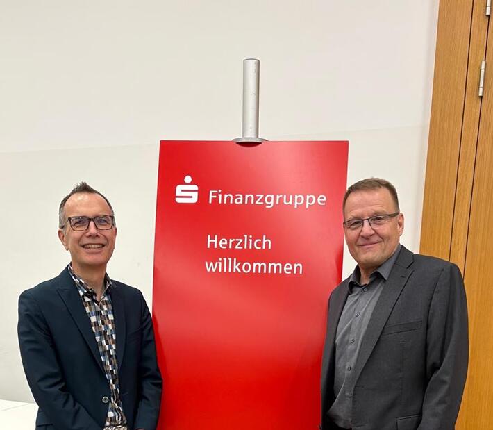 Zwei Männer stehen vor einem Roll-up der Sparkassen-Finanzgruppe