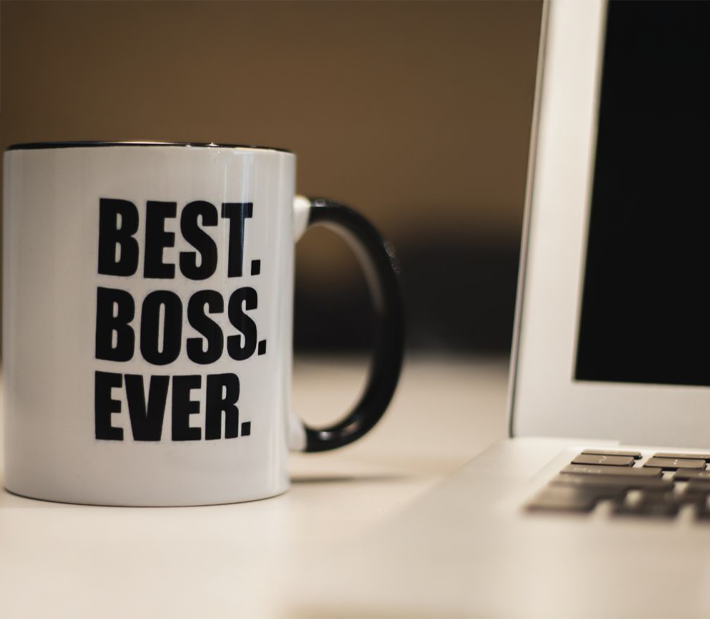 Kaffeetasse mit Aufschrift "Best Boss Ever" neben einem Laptop auf einem Schreibtisch