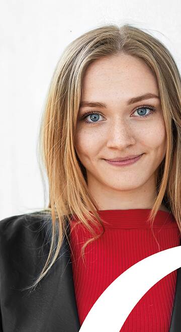 blonde Frau lehnt an einer Hauswand und lächelt