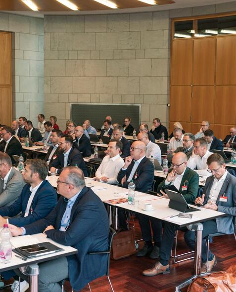 Teilnehmende vom Forum Firmenkundengeschäft sitzen an Tischreihen in der Aula