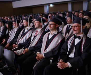 Eine Gruppe Master-Absolventen sitzt in einem Saal auf Stühlen