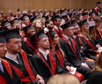 Eine Gruppe Bachelor-Absolventen sitzt in einem Saal auf Stühlen