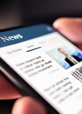 Smartphone liegt in einer Hand und zeigt Newsartikel an