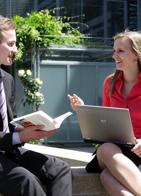 Ein Mann mit Buch und eine Frau mit Laptop unterhalten sich