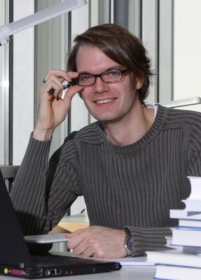 Ein Mann sitzt mit Laptop und Büchern am Schreibtisch