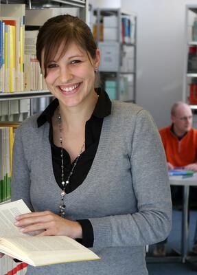 Eine Frau hält ein Buch in den Händen und lächelt in die Kamera