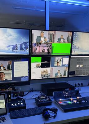Mehrere PC-Bildschirme auf einem Schreibtisch zeigen verschiedene Ansichten eines Online-Meetings