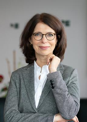 Anne Böhm-Dries mit verschränkten Armen in einem modernen Büroumfeld.
