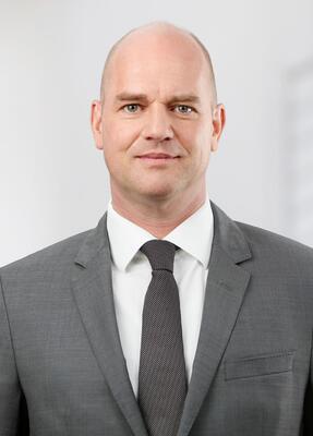 Ein Mann im Anzuig steht in einem Büro und lächelt
