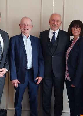 5 Personen in Business Kleidung stehen vor einer Wand und lächeln
