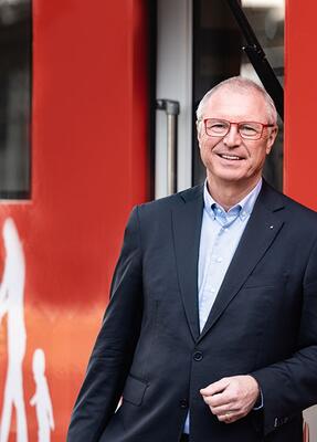 Ein Mann im Anzug steht vor einem roten Hintergrund