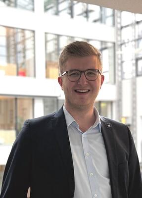 Ein junger Mann im Anzug lächelt in die Kamera