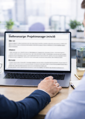 Zwei Männer schauen auf einen Monitor, der eine Stellenausschreibung zeigt.