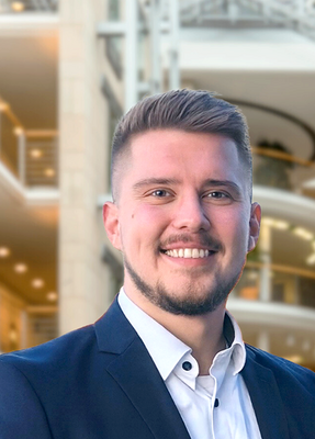 Ein junger Mann im Anzug lächelt in die Kamera