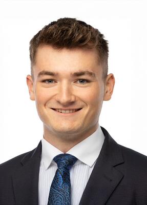 Student im Business Management im Anzug mit Krawatte lächelnd vor weißem Hintergrund.