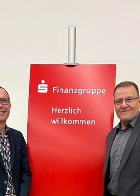 Zwei Männer stehen vor einem Roll-up der Sparkassen-Finanzgruppe