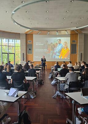 Blick in die Aula der Hochschule mit sitzenden jungen Menschen und dem Rektor
