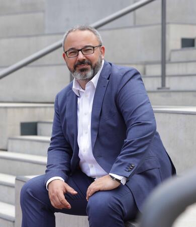 Prof. Dr. Denis Bagbasi sitzt auf einer Treppe und trägt einen blauen Anzug.