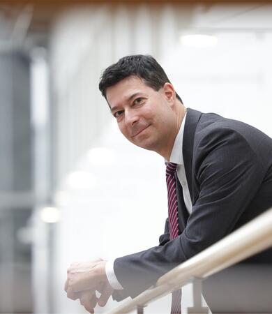 Professor André Lucas steht an einem Holzgeländer in einem modernen Gebäude.