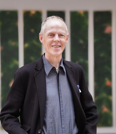 Professor Dirk Neuhaus steht in einem Raum vor drei vertikalen Wandbildern.