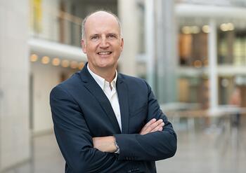 Ein Mann im Anzug steht in einem Foyer und lächelt in die Kamera