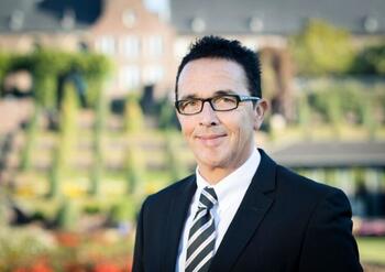 Prof. Dr. Christoph Landscheidt im Anzug mit gestreifter Krawatte vor einer grünen Gartenlandschaft.