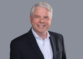 Stefan Zurawka, Vertriebsleiter im Internationalen Geschäft, steht lächelnd in Anzug vor grauem Hintergrund.