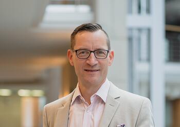Prof. Dr. Mike Schneider lehnt am Geländer und schaut direkt in die Kamera