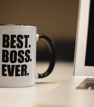 Kaffeetasse mit Aufschrift "Best Boss Ever" neben einem Laptop auf einem Schreibtisch