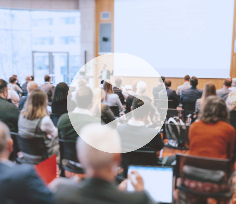 Publikum in Rückenansicht bei Seminar mit großem Playbutton als Videovorschau
