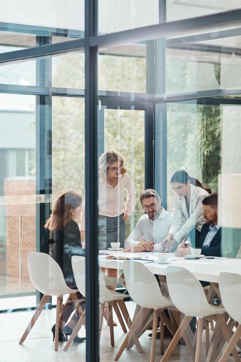Team mit Führungskraft im Austausch am Konferenztisch hinter Scheiben